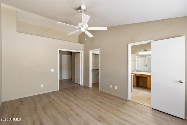 unfurnished bedroom featuring vaulted ceiling, a spacious closet, connected bathroom, and light wood-style flooring