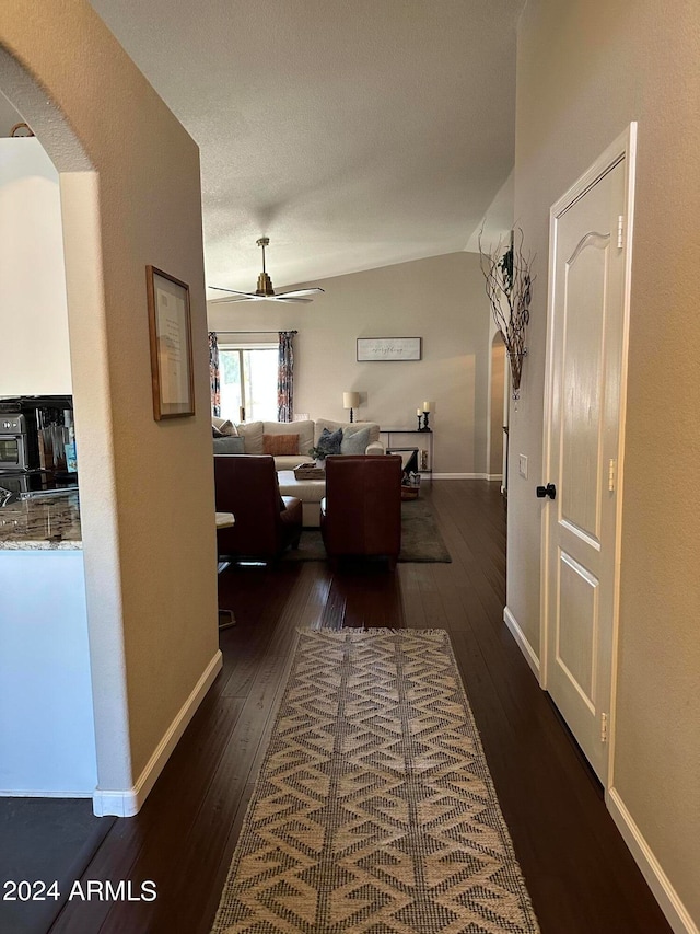 hallway with a textured ceiling, vaulted ceiling, and dark wood-type flooring