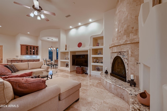 living room featuring built in shelves, ceiling fan with notable chandelier, a fireplace, and a high ceiling