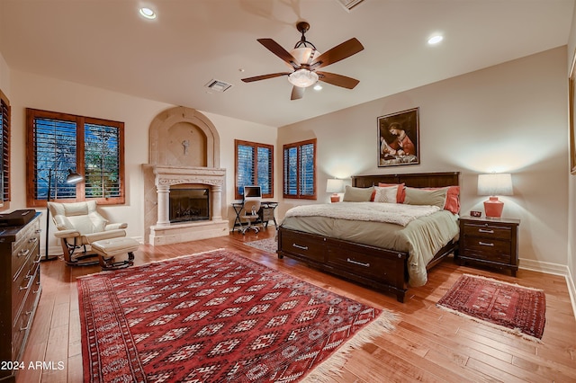 bedroom with a high end fireplace, ceiling fan, and light hardwood / wood-style floors