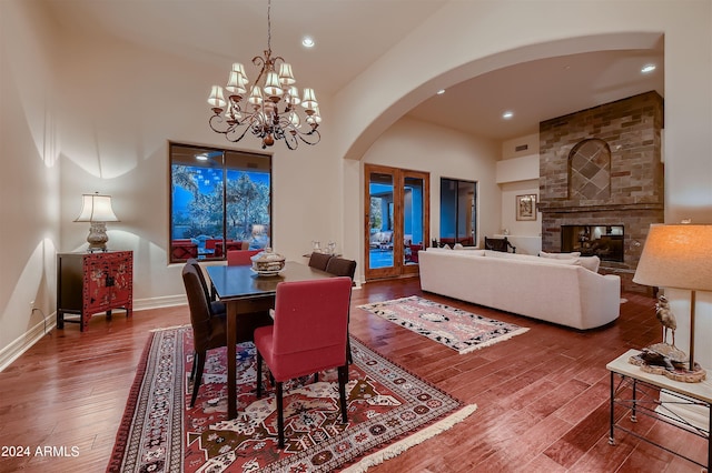 dining room with a notable chandelier, a fireplace, hardwood / wood-style floors, and a high ceiling