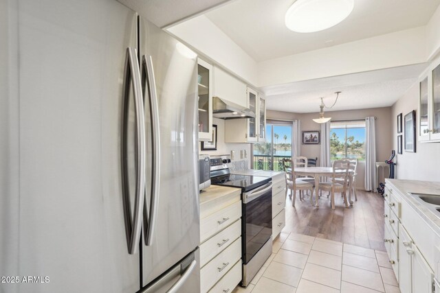 kitchen with appliances with stainless steel finishes, light countertops, wall chimney range hood, and light tile patterned flooring