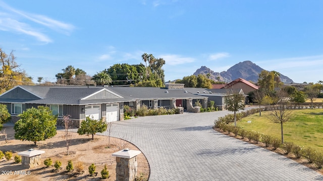 single story home featuring decorative driveway, an attached garage, a mountain view, and a front yard