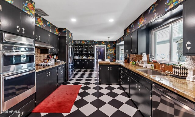 kitchen featuring a sink, dark floors, under cabinet range hood, and dark cabinets