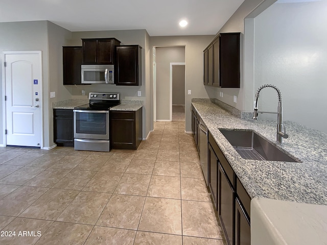 kitchen featuring light tile patterned floors, stainless steel appliances, light stone counters, and a sink