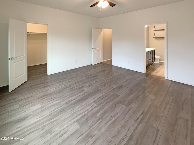 unfurnished bedroom featuring dark wood-style floors, ceiling fan, ensuite bathroom, a spacious closet, and a closet