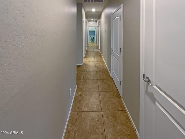 hallway with tile patterned flooring, visible vents, a textured wall, and baseboards