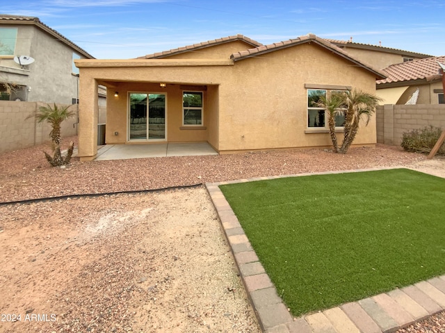 rear view of house with a yard, a patio, stucco siding, a fenced backyard, and a tiled roof