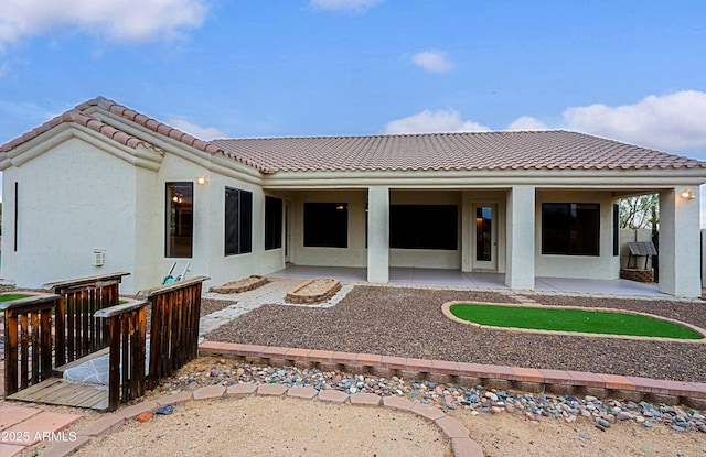 rear view of property with a patio area, a tile roof, and stucco siding