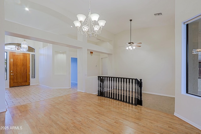 unfurnished room with visible vents, a towering ceiling, light wood-style floors, a chandelier, and baseboards