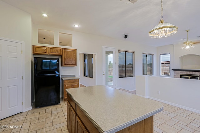 kitchen featuring a fireplace, open floor plan, light countertops, freestanding refrigerator, and brown cabinetry