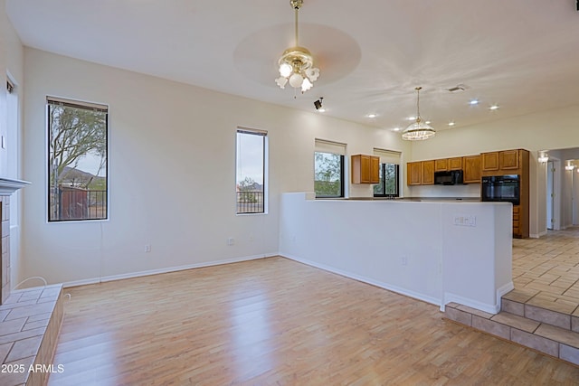 kitchen with light wood finished floors, brown cabinets, decorative light fixtures, black appliances, and ceiling fan with notable chandelier