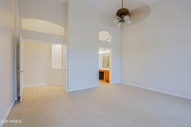 empty room featuring ceiling fan, a high ceiling, baseboards, and light colored carpet