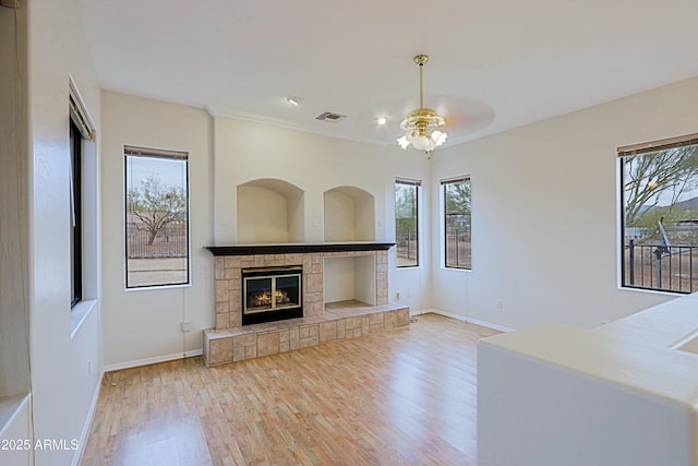 unfurnished living room featuring baseboards, visible vents, a tiled fireplace, and wood finished floors