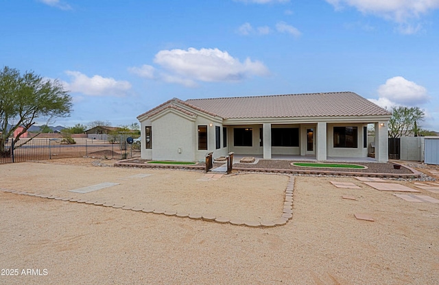 view of front facade with a patio area, a tile roof, fence, and stucco siding