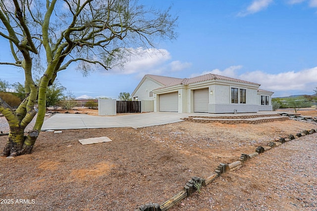 view of front of home featuring an attached garage, fence, concrete driveway, a tiled roof, and stucco siding