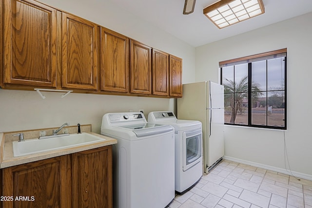 clothes washing area featuring ceiling fan, a sink, baseboards, cabinet space, and washing machine and clothes dryer