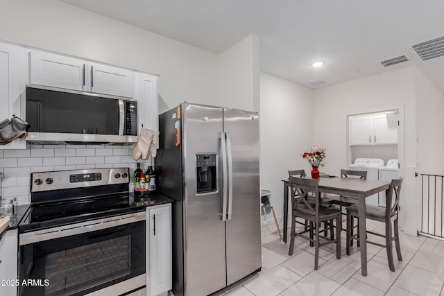 kitchen featuring washer and clothes dryer, visible vents, decorative backsplash, appliances with stainless steel finishes, and white cabinetry