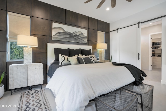 bedroom featuring ceiling fan, a barn door, a spacious closet, light tile patterned flooring, and a closet