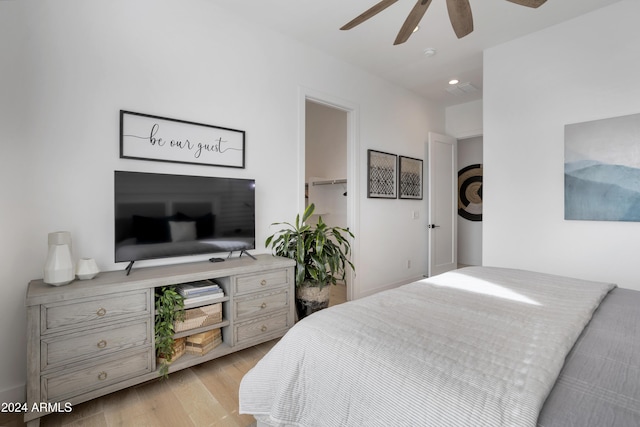 bedroom with ceiling fan, a walk in closet, and light wood-type flooring