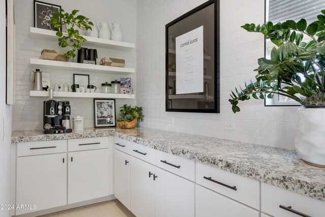 bar with white cabinets, backsplash, and light stone counters