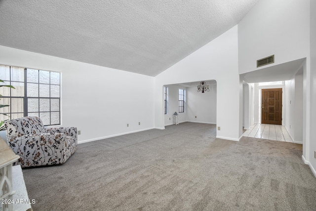 unfurnished living room featuring light carpet, high vaulted ceiling, a textured ceiling, and a notable chandelier