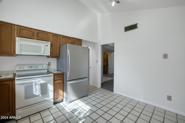 kitchen featuring light tile patterned floors, high vaulted ceiling, and white appliances