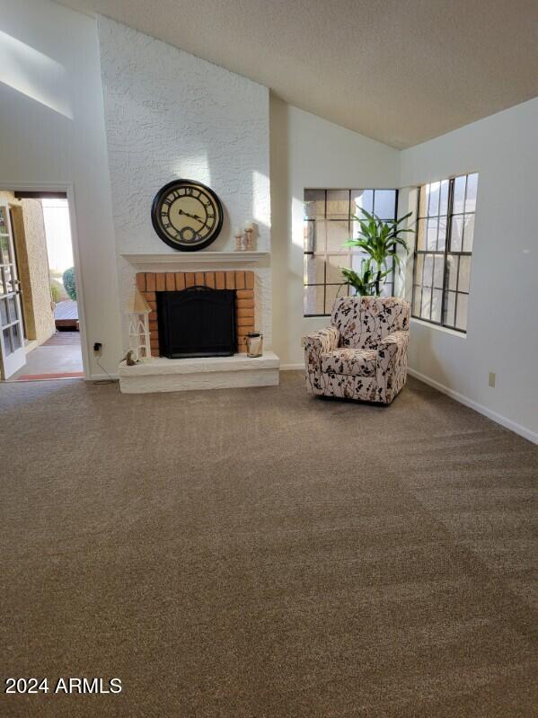 unfurnished living room with a textured ceiling, carpet floors, a fireplace, and high vaulted ceiling