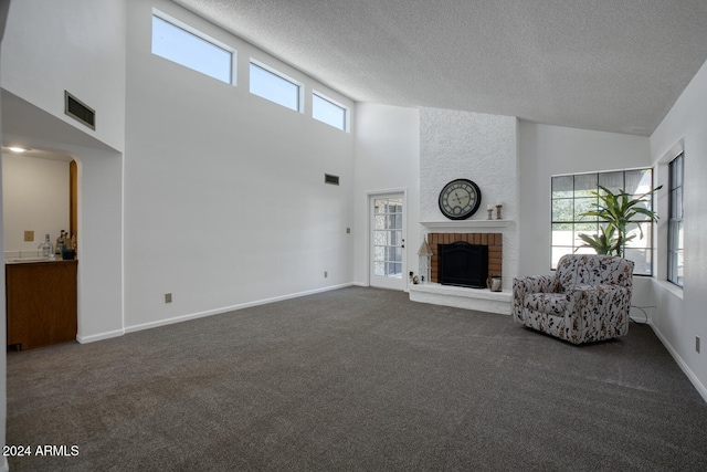 unfurnished living room with dark colored carpet, a towering ceiling, a textured ceiling, and a brick fireplace