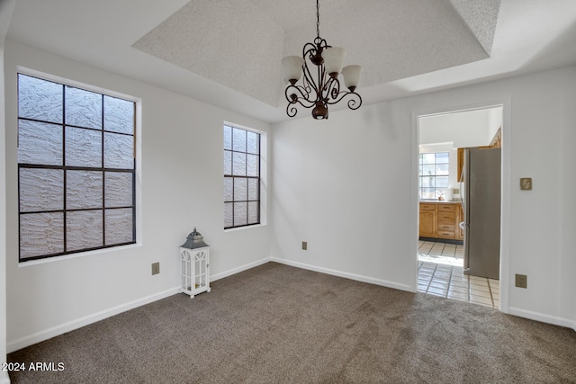 empty room with carpet, a textured ceiling, a wealth of natural light, and a notable chandelier