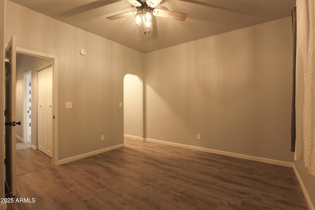 unfurnished room with dark wood-style floors, baseboards, arched walkways, and a ceiling fan