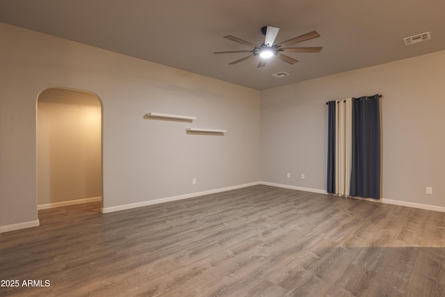 spare room featuring arched walkways, wood finished floors, visible vents, baseboards, and a ceiling fan