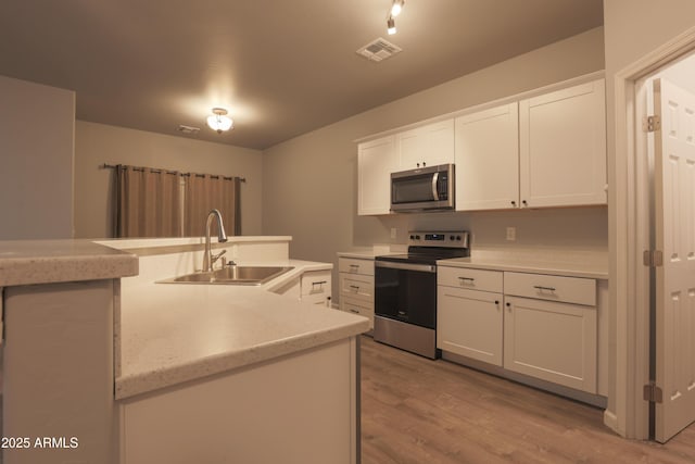 kitchen with stainless steel appliances, white cabinetry, sink, and light wood-type flooring