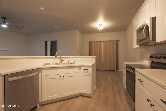 kitchen with light countertops, appliances with stainless steel finishes, white cabinets, a sink, and light wood-type flooring