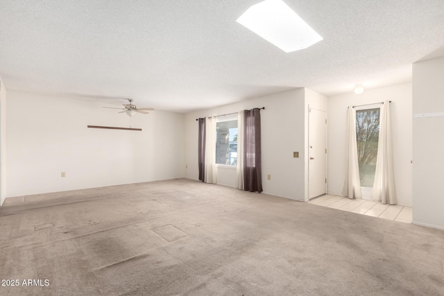 carpeted spare room featuring ceiling fan, a skylight, and a textured ceiling