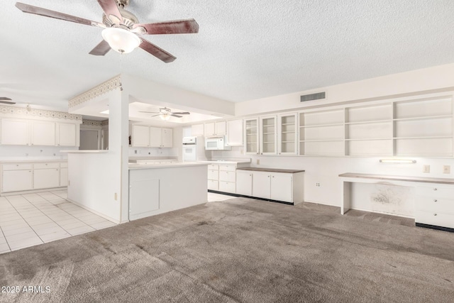 kitchen featuring white cabinets, a center island, light colored carpet, a textured ceiling, and white appliances