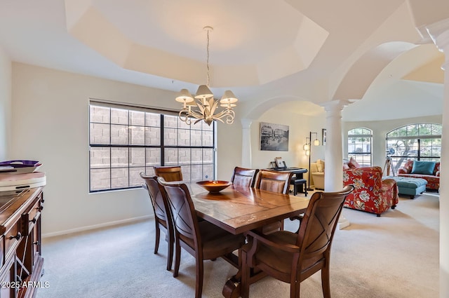 dining space with a raised ceiling, light colored carpet, a chandelier, and ornate columns