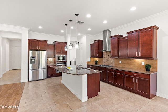 kitchen with stainless steel appliances, a sink, wall chimney exhaust hood, dark stone counters, and an island with sink