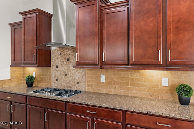 kitchen featuring stainless steel gas stovetop, wall chimney exhaust hood, light stone counters, and dark brown cabinets