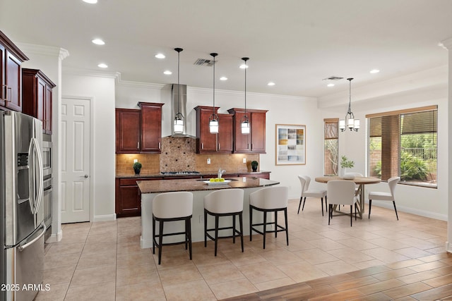 kitchen featuring stainless steel appliances, wall chimney exhaust hood, tasteful backsplash, ornamental molding, and an island with sink