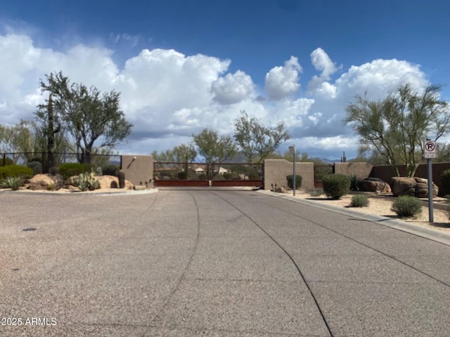 view of asphalt street featuring a gate, curbs, traffic signs, and a gated entry