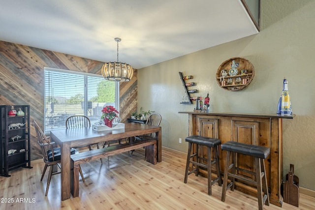 dining space with light hardwood / wood-style floors, wood walls, and an inviting chandelier