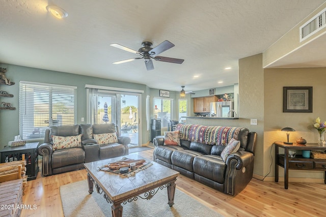 living room featuring ceiling fan, a textured ceiling, and light wood-type flooring