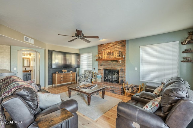 living room featuring ceiling fan, wood-type flooring, and a brick fireplace