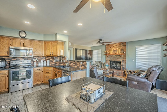 kitchen with appliances with stainless steel finishes, decorative backsplash, sink, light tile patterned flooring, and a brick fireplace