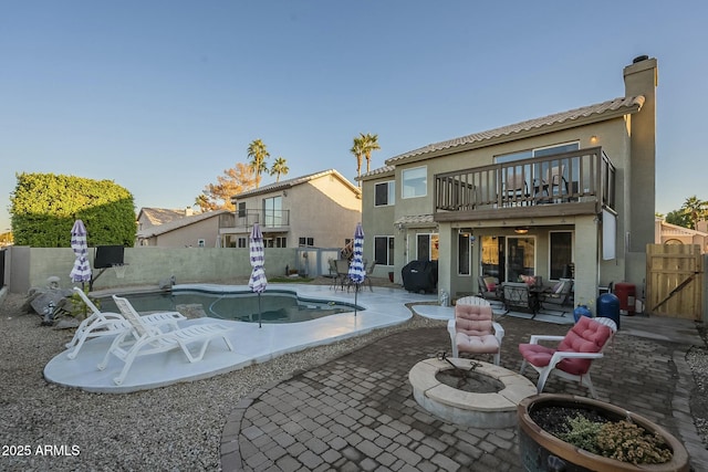 back of property featuring an outdoor living space with a fire pit, a patio, a balcony, and a fenced in pool