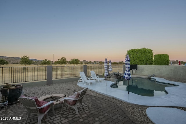 patio terrace at dusk featuring a fenced in pool and a fire pit