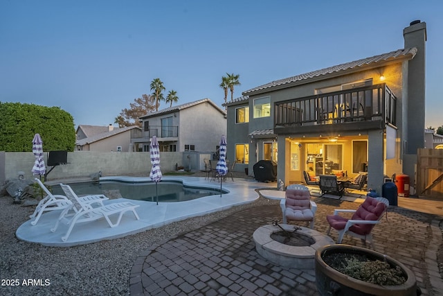 back house at dusk featuring a balcony, an outdoor fire pit, a fenced in pool, and a patio