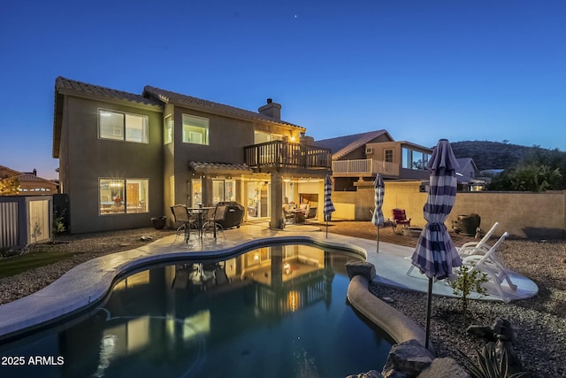 back house at dusk with a balcony, a patio area, a fenced in pool, and a pergola