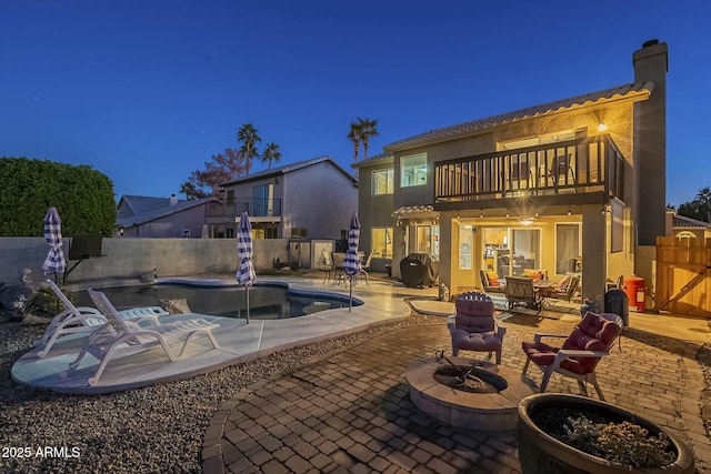 rear view of property with a balcony, a patio area, a fenced in pool, and a fire pit